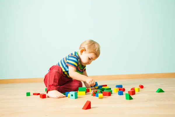 เด็กน่ารักนั่งอยู่บนพื้น สร้างหอของเล่นพัง — ภาพถ่ายสต็อก