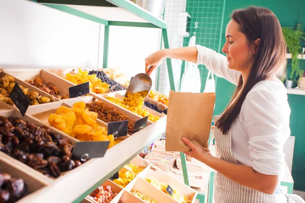 Mujer joven vendedor paquetes de frutas secas en la tienda de comestibles —  Fotos de Stock