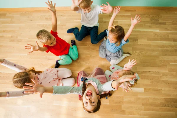 Весёлые детишки с поднятыми руками сидят на полу — стоковое фото