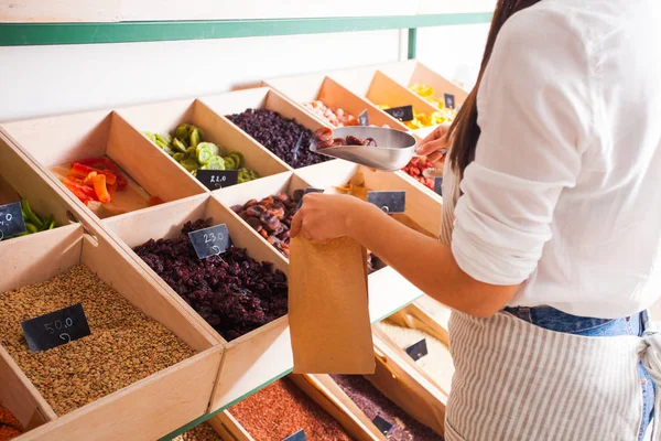 Young woman seller packs dried fruits in the grocery shop