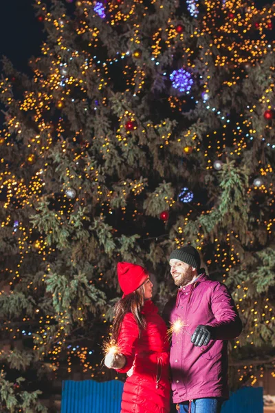 Pareja con bengalas delante de un gran árbol de Navidad — Foto de Stock