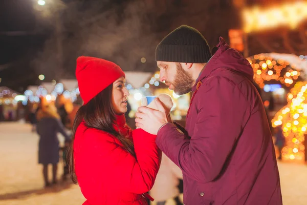 Alegre pareja bebiendo vino caliente de una taza en la feria de Navidad — Foto de Stock