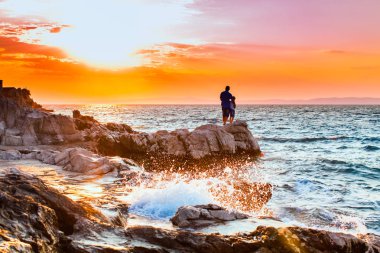 Yung adam bir kaya üzerinde duran ve deniz günbatımı bakarak
