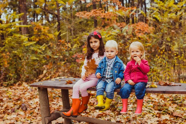Tres niños sentados en el banco y jugando —  Fotos de Stock