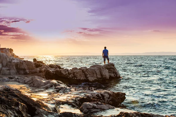 Yung adam bir kaya üzerinde duran ve deniz günbatımı bakarak