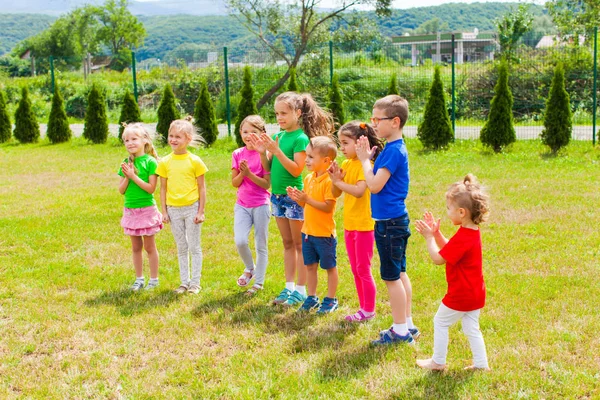 Grupp barn klappar händerna på det gröna gräset — Stockfoto