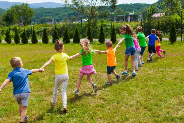 I bambini giocano tenendosi per mano sull'erba verde, vista posteriore — Foto Stock