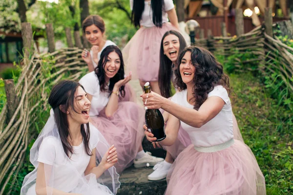 Bride and bridesmaids opening bottle of champagne, sitting on steps — Stock Photo, Image