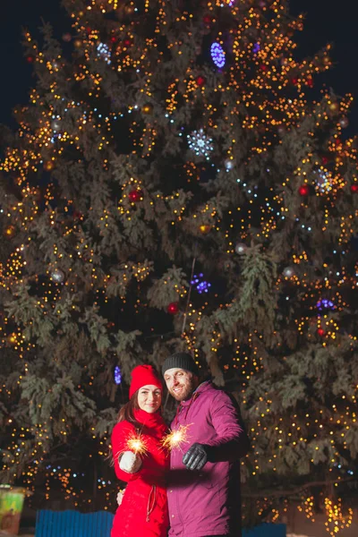 Grote versierde kerstboom met Jong paar staande in de buurt — Stockfoto