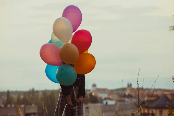 Girl with colorful balloons walking on the sunset