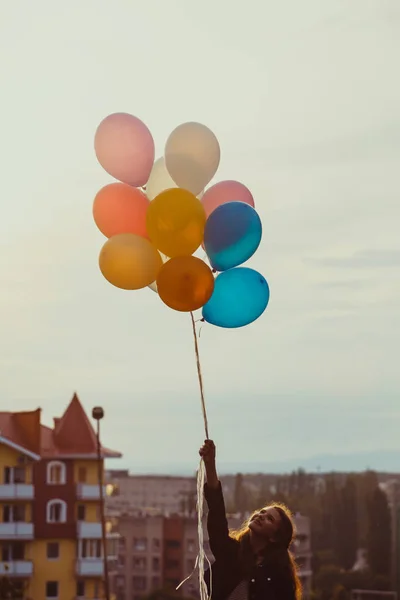 Girl with colorful balloons walking on the sunset