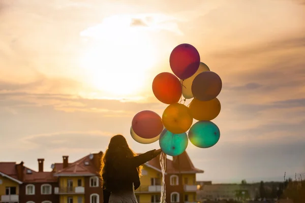 Menina com balões coloridos andando no pôr do sol — Fotografia de Stock