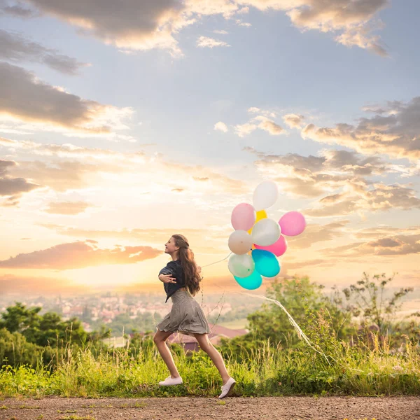 Chica con globos de colores en la puesta del sol — Foto de Stock