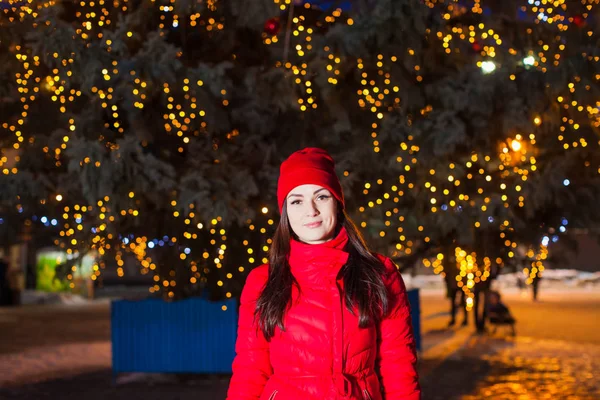 城市圣诞树下穿红色外套的迷人女人 — 图库照片