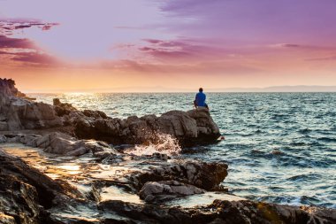 Yung adam bir kaya üzerinde duran ve deniz günbatımı bakarak