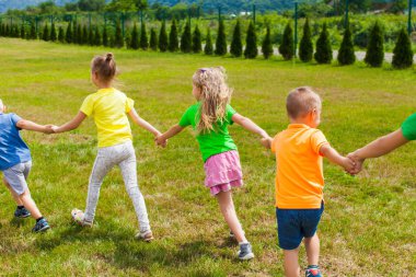 Çocuklar el ele tutuşup yeşil çimenlikte oynuyorlar.