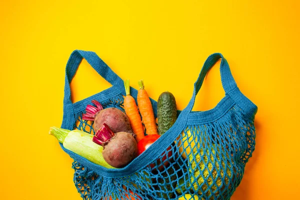 Vegetables in mesh cotton bag on yellow background