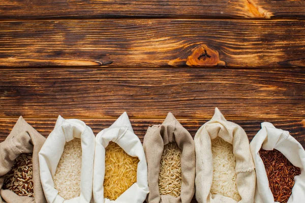 Diferentes tipos de arroz em sacos têxteis em fundo de madeira — Fotografia de Stock