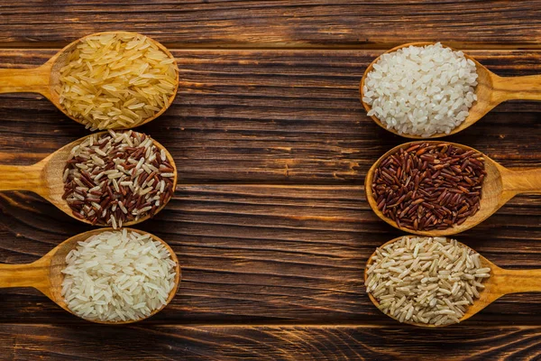 Colheres de madeira com diferentes tipos de arroz no fundo de madeira — Fotografia de Stock