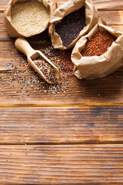 Witte, rode en zwarte quinoa in papieren zakken op de houten tafel — Stockfoto