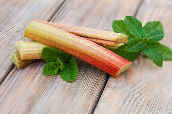 Rabarbaro fresco e foglie di menta su un tavolo di legno — Foto Stock