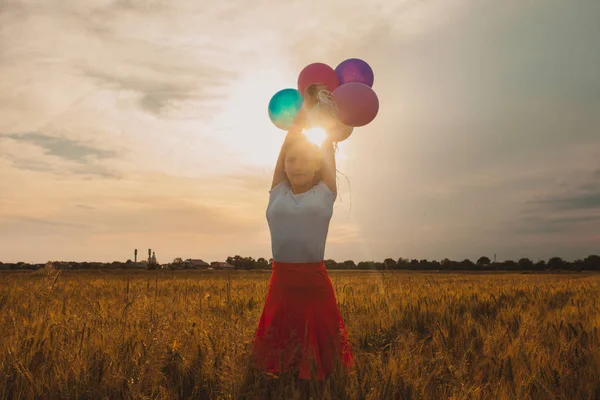 Menina com balões no campo de trigo e luz do sol no pôr do sol — Fotografia de Stock