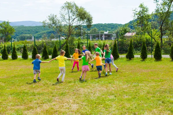 Дети бегут, держа руки на зеленой лужайке — стоковое фото