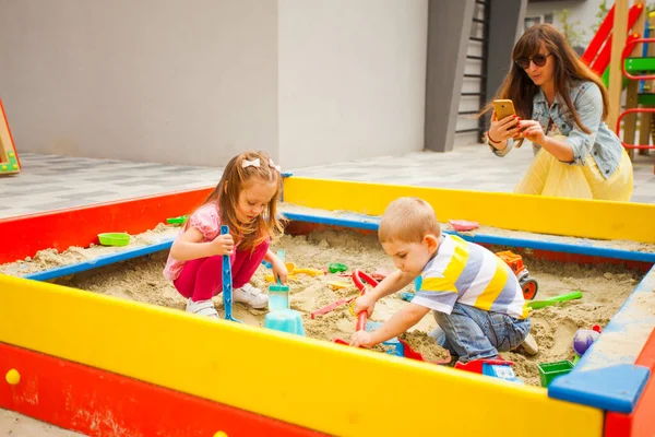 Mãe tirando foto no smartphone, as crianças brincam na sandbox — Fotografia de Stock