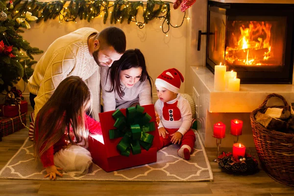 Szczęśliwa rodzina otwarta świąteczne oświetlenie pudełko obok choinki. — Zdjęcie stockowe
