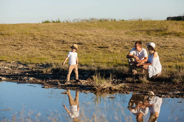 一家人走在池塘边，男孩扔鹅卵石 — 图库照片