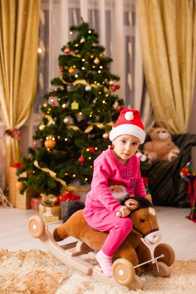 Menina feliz montando um cavalo na frente da árvore de Natal em casa . — Fotografia de Stock