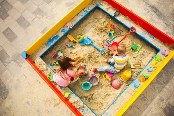 Enfants heureux jouant avec des jouets dans un grand bac à sable à l'extérieur, vue de dessus — Photo