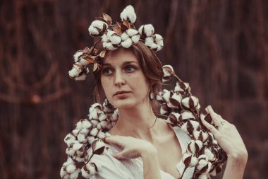 Etrafında pamuk çiçekleri olan harika saç stili olan hassas bir kadın.
