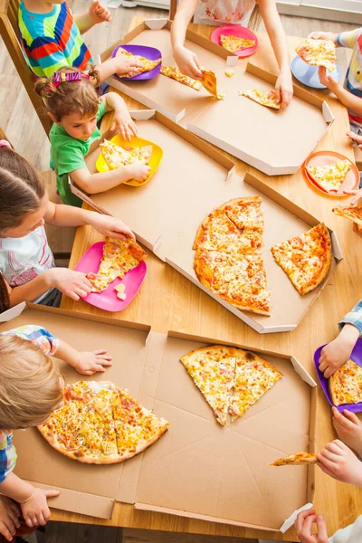 Imagem de vista superior de crianças tirar fatias de pizza da caixa na cozinha . — Fotografia de Stock