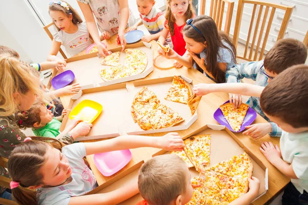 Crianças felizes comendo pizza e se divertindo juntos . — Fotografia de Stock