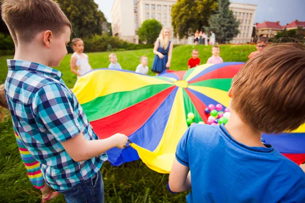 Glückliche Kinder spielen aktives Spiel mit buntem Fallschirm — Stockfoto