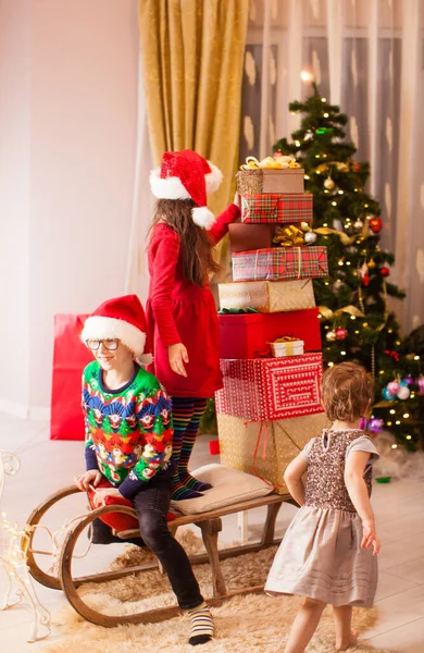 Fröhliche lustige Kinder, die einen Schlitten voller Weihnachtsgeschenke ziehen — Stockfoto