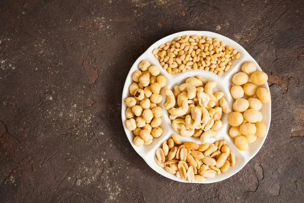 Big plate full of various nuts over black background, copy space — Stock Photo, Image