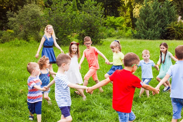 Boldog gyerekek táncolnak körbe-körbe a zöld gyepen a parkban — Stock Fotó