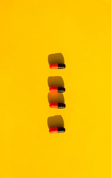 Negro píldoras rojas en el fondo amarillo — Foto de Stock