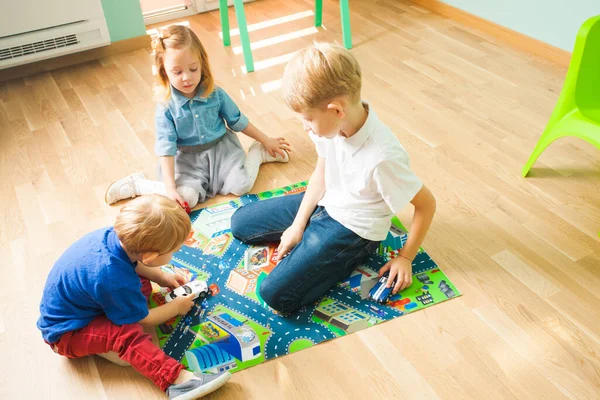 Kinder spielen mit Autos auf einem Mottoteppich. Kinder zu Hause oder in der Kita. — Stockfoto