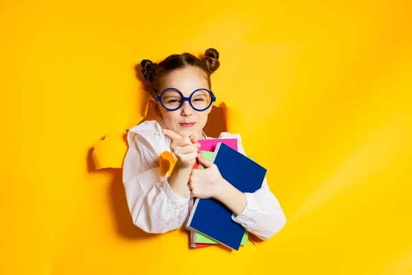 Chytrá školačka se dívá skrz díru ve žlutém papíru. Zpátky do školy. — Stock fotografie