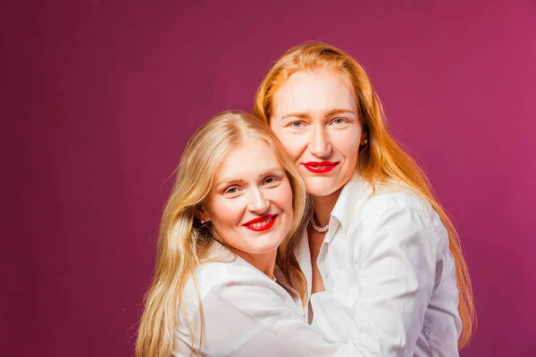 Duas irmãs bonitas abraçando no fundo roxo — Fotografia de Stock