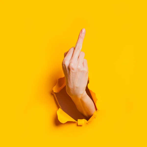 Mano femenina mostrando gesto que significa follarte o follar a través del agujero en el fondo de papel amarillo . — Foto de Stock