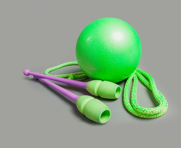 Professional equipment for gymnastics workout on grey background. Green ball, mace and rope for gymnastics. — Stock Photo, Image