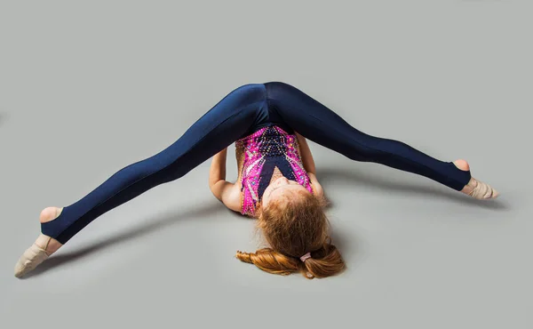 Ung gymnastisk flicka sträcker på benen på ett golv — Stockfoto