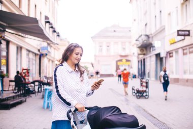 Şehir sokağında, bebek arabası ve telefonu olan modern bir anne.