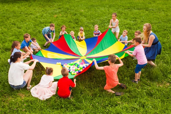 Niños alegres jugando con paracaídas multicolor y bolas pequeñas —  Fotos de Stock