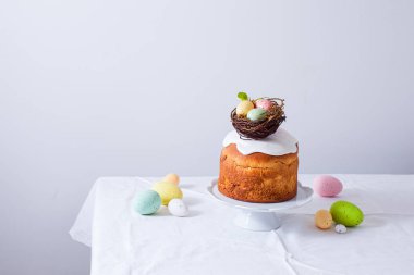 Yuvalı Paskalya pastası ve beyaz bir masada renkli yumurtalar.