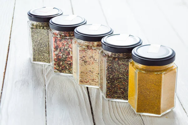 Glass jars with some spices on white wooden surface. — Stock Photo, Image